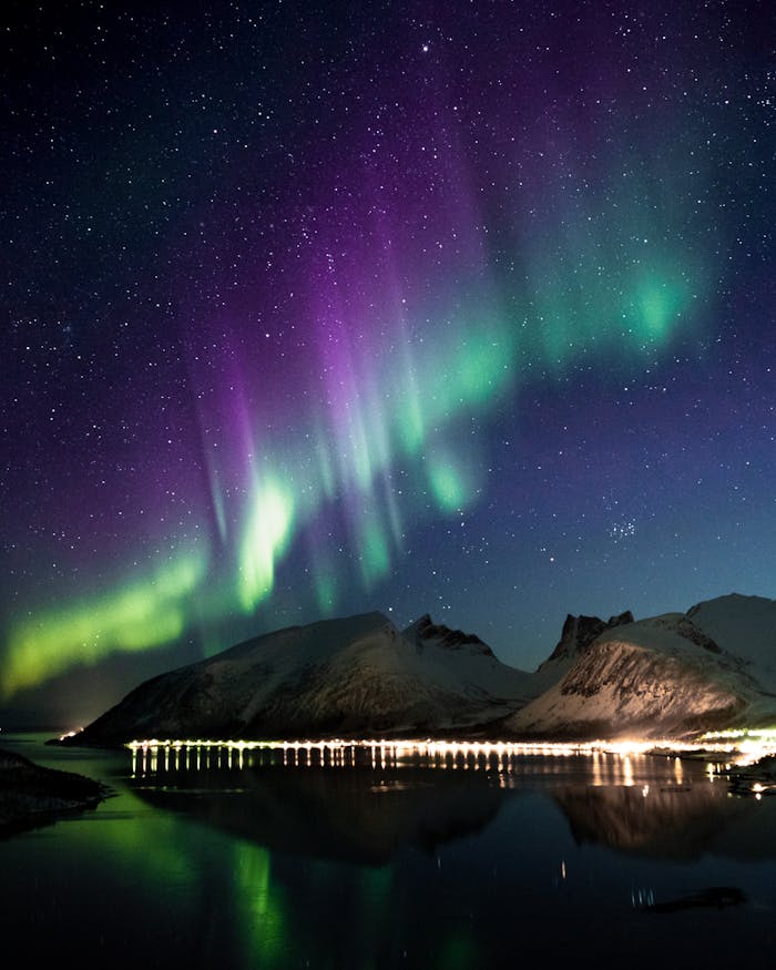 Captivating view of the Aurora Borealis dancing over snow-covered mountains reflecting on a serene lake.